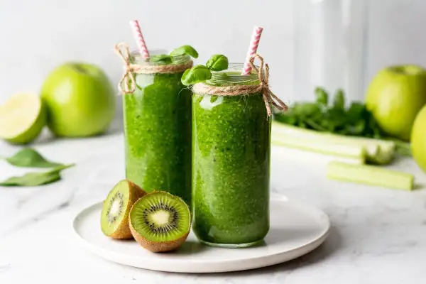 Dwa zielone koktajle w słoikach z kiwi, jabłkami i słomkami.